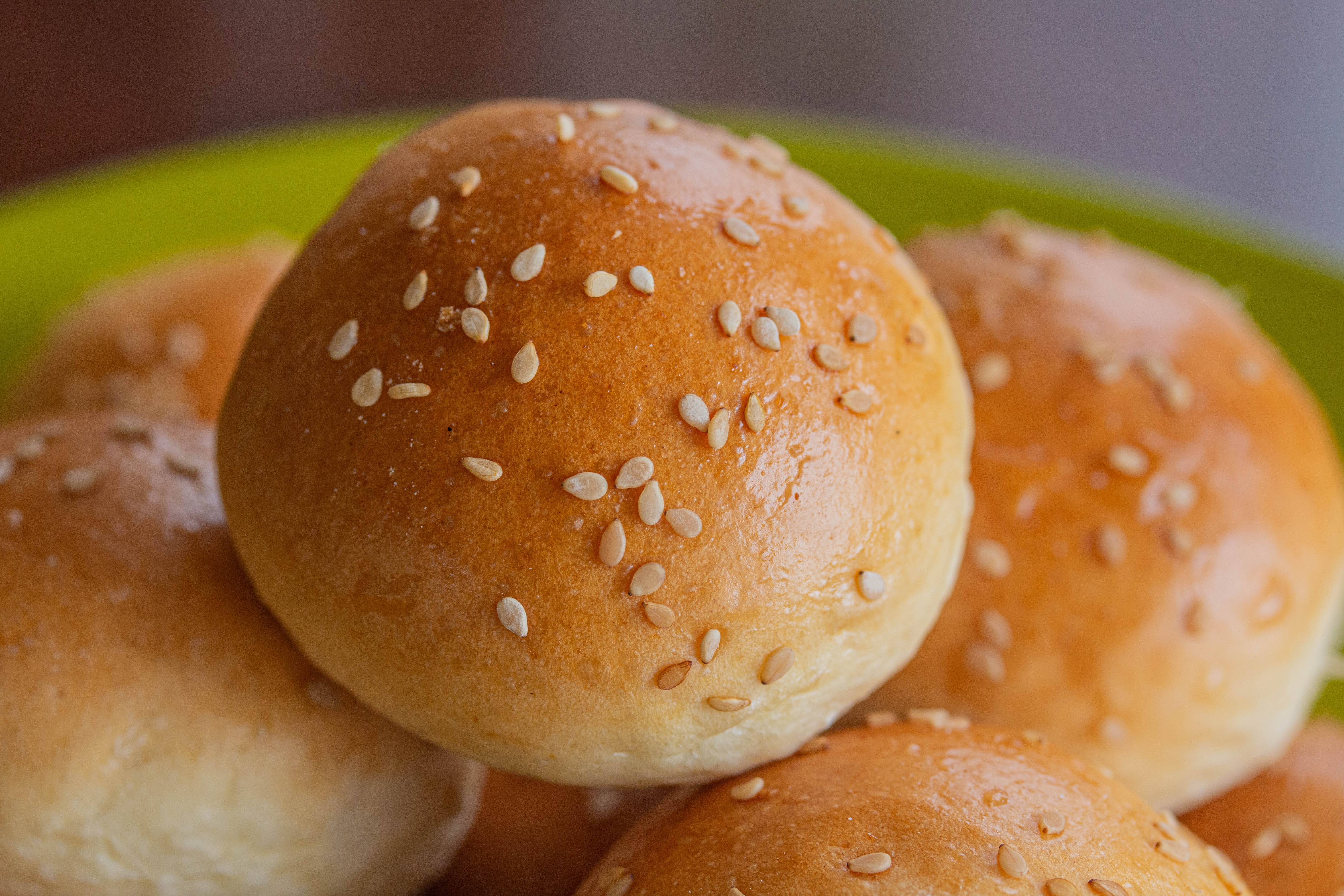 A bowl of small sesame seed buns with bright specular highlights coming from two sources.